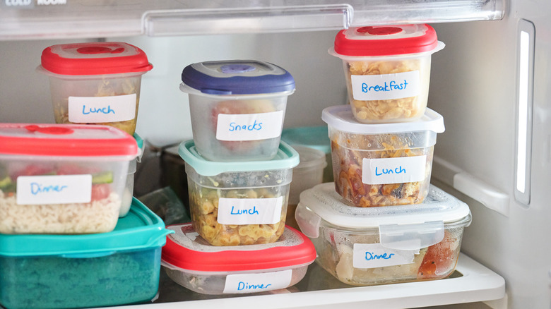 Plastic containers of food labeled for different meals stacked on a shelf inside of a refrigerator