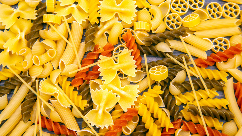 A pile of various shapes of dry pasta on a wooden table