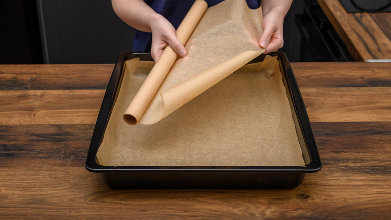 A woman lines a black baking pan with parchment paper