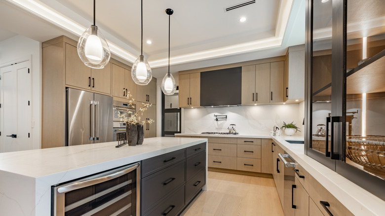 A sleek kitchen is decorated in neutral colors with glass pantry doors.