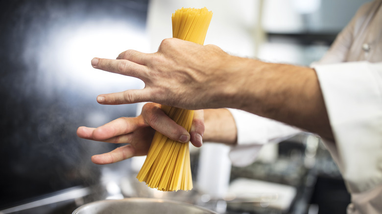 Chef with hands around uncooked spaghetti noodles
