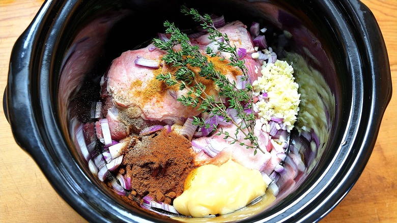 Raw pork chops in a slow cooker with raw onions, chopped garlic, and fresh herbs