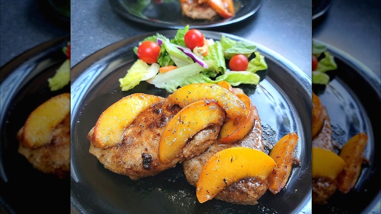 Cooked pork chops with peaches and side salads on black plates