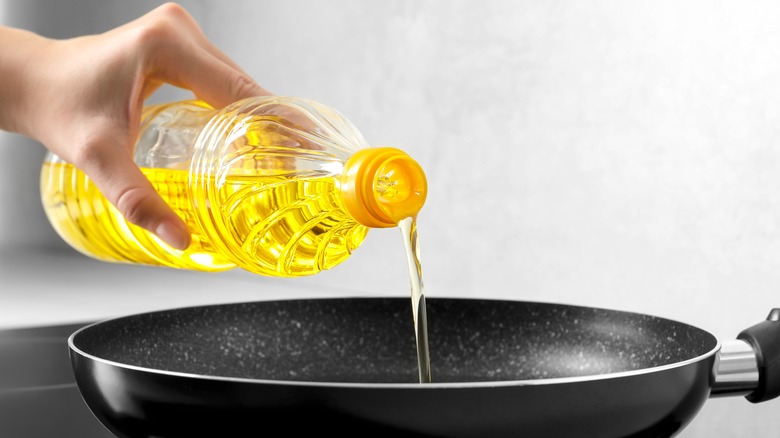 Person pouring oil into pan.