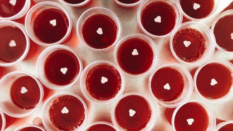Top-down view of red Jell-O shots with small white hearts in plastic cups