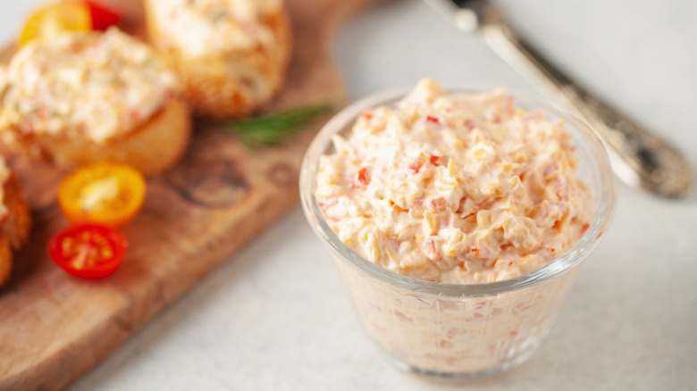 Pimento cheese in a small bowl in front of a cutting board with food