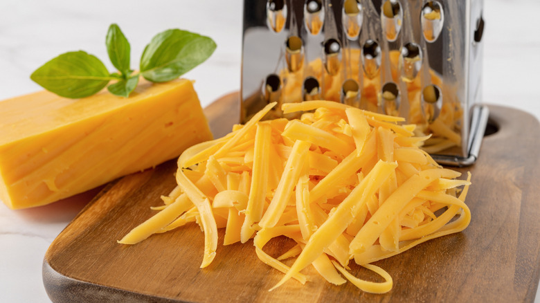 Grated cheese in front of a grater on a cutting board