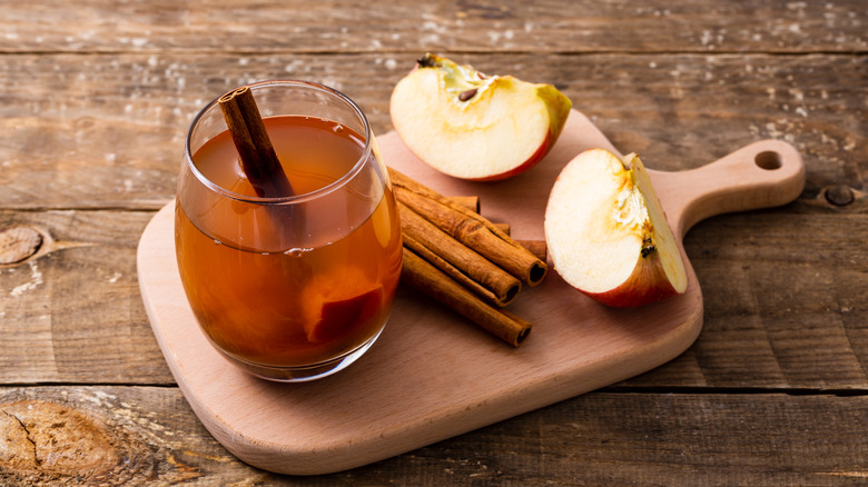 A glass of apple cider displayed on a cutting board