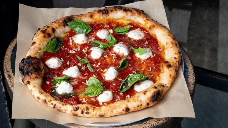 Pizza with tomato sauce, mozzarella, and basil on patchment paper