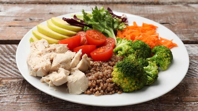 Plate of chicken, quinoa, broccoli, fruit, and vegetables