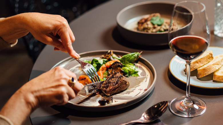 Hands cutting a steak.