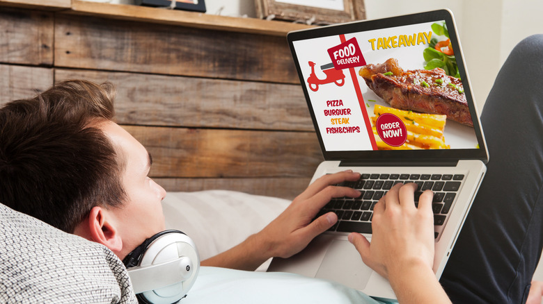 Man placing order through a food delivery website on laptop while lying down.