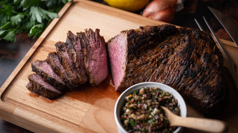 A tri-tip steak is sliced on a cutting board to reveal its pink interior.
