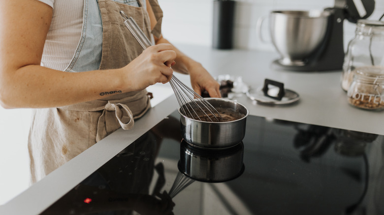 Woman with apron whisking food in pot on induction stovetop