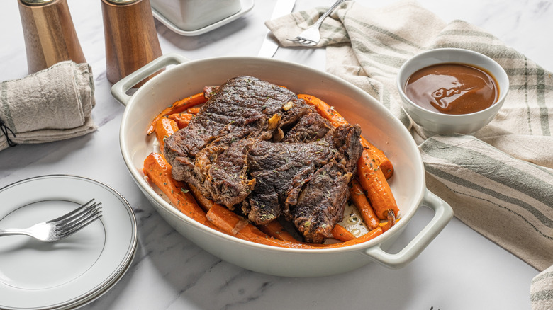 A juicy pot roast served with carrots and a bowl of gravy on the side