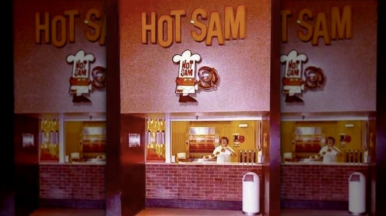 A worker stands behind the counter at a Hot Sam location, displaying some of the brand's signature soft pretzels.