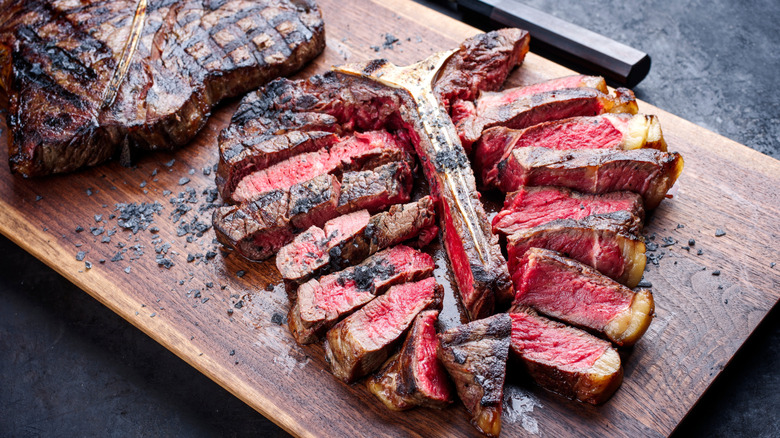 A juicy porterhouse steak with charred edges placed on a wooden board.