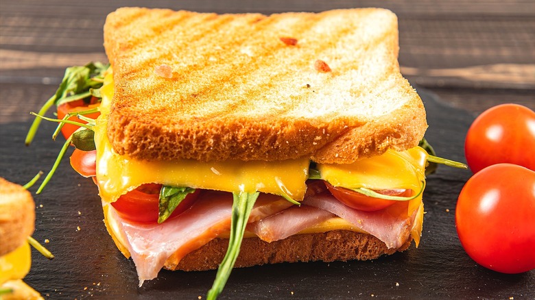 Toasted ham and cheese sandwich with sliced tomato and greens