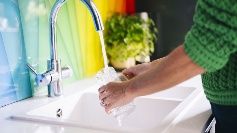 person washing glass at a white kitchen sink
