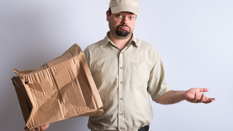 Unrepentant delivery man holding smashed box