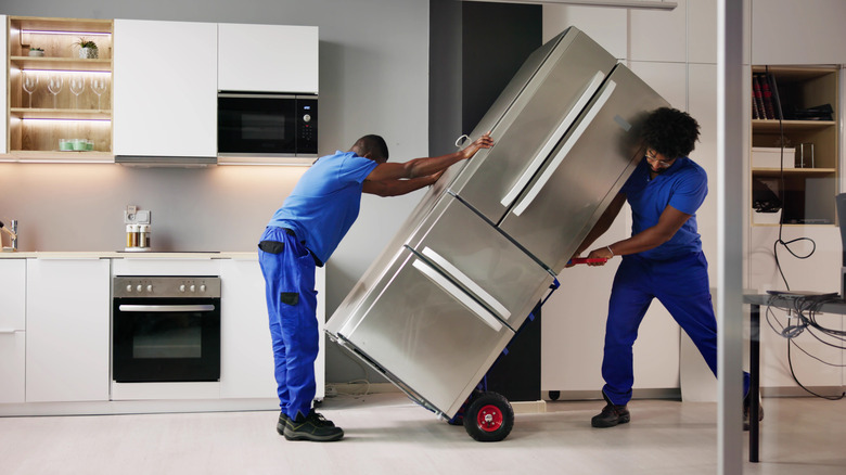Two men delivering refrigerator to kitchen