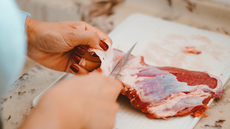 person cutting fat off of a hunk of raw meat