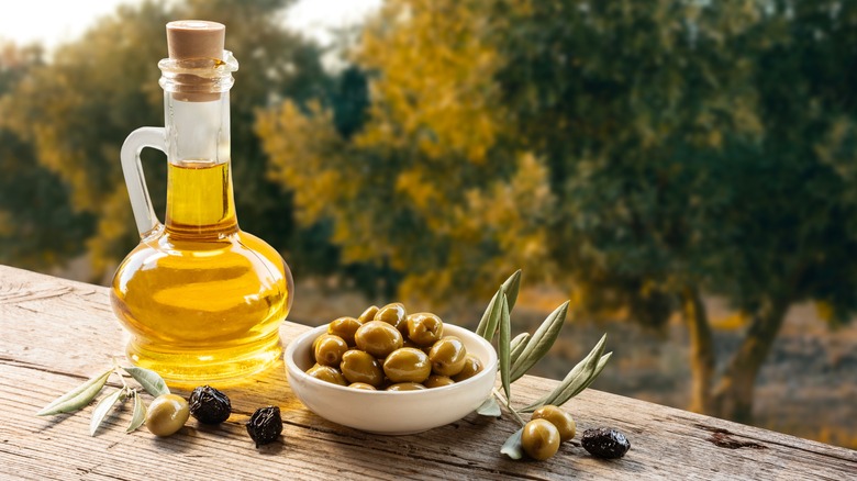 glass decanter of olive oil on a wooden table outdoors with olives on the side