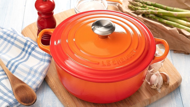 Le Creuset orange enameled cast iron pot on wooden cutting board