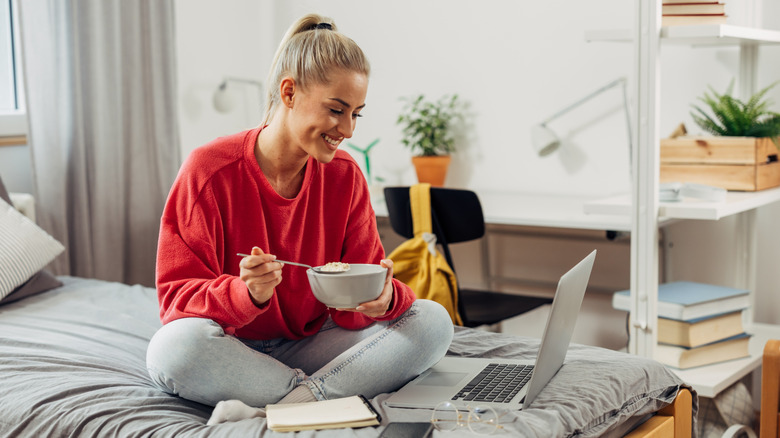 College student eating breakfast while working in her dorm room