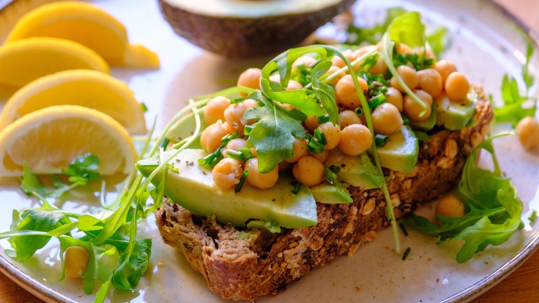 Avocado toast topped with roasted chickpeas, fresh arugula, and mixed seeds.