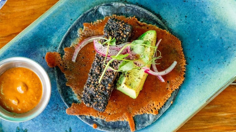 A seared tuna taco on a blue tray with dish of sauce on the side at Abulón Antojería del Mar