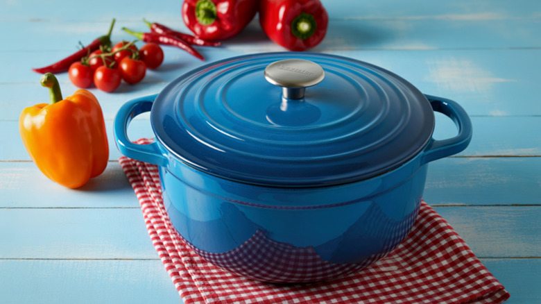 Blue dutch oven on a checkered red and white napkin with peppers and tomatoes in the background