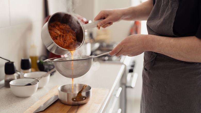 A cook pouring liquid out of a pot of shrimp into a strainer