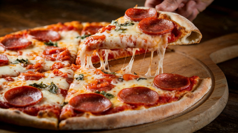 A hand pulling a cheesy slice of homemade pizza from a pizza paddle