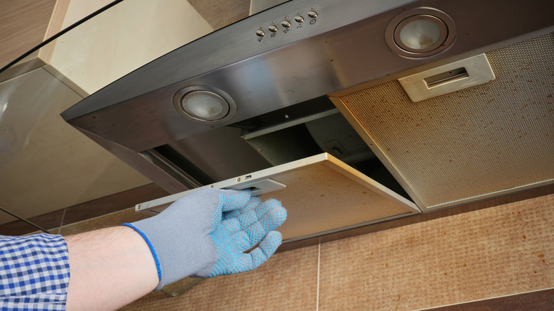 person wearing gloves opens filter in a range hood