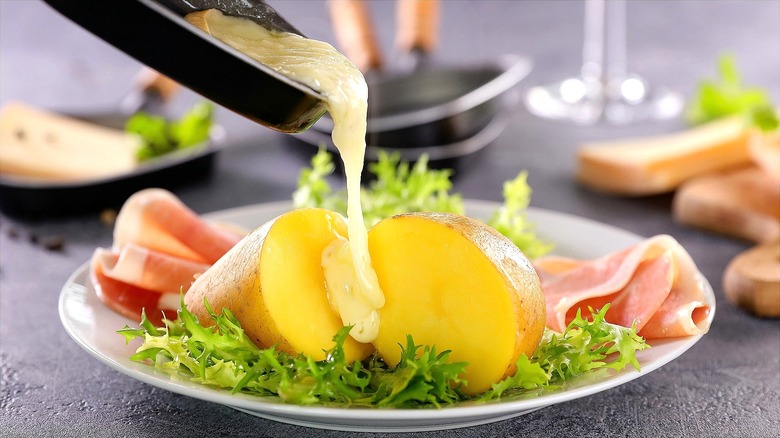 Melted raclette cheese being poured onto a cooked sliced potato