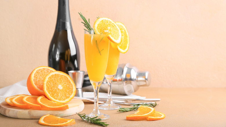 Mimosas are served in Champagne flutes with oranges arranged around the glasses.