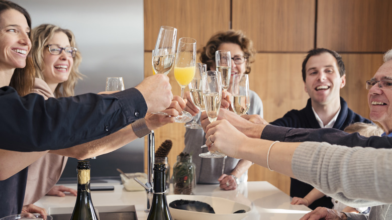 People gathered around a table toast with mimosas and sparkling white wine.