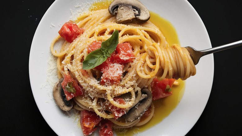White plate with spaghetti, tomatoes, mushrooms, and fork