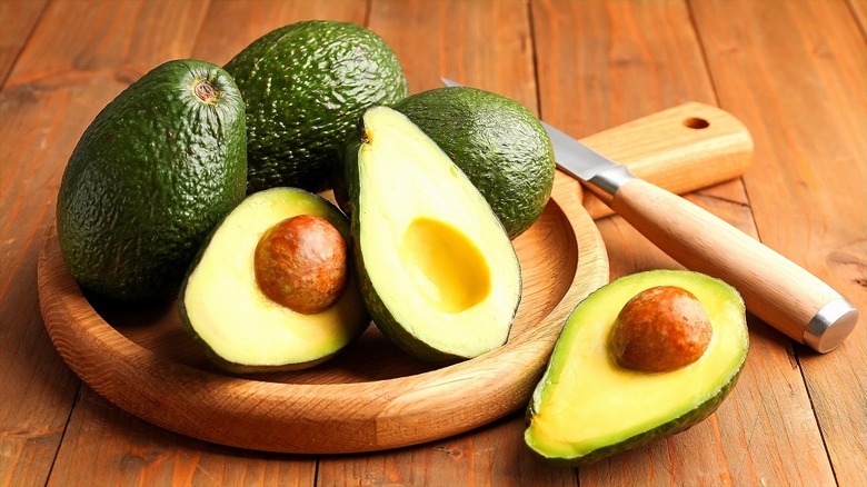 Whole and halved avocados on a round wooden serving plate with handle