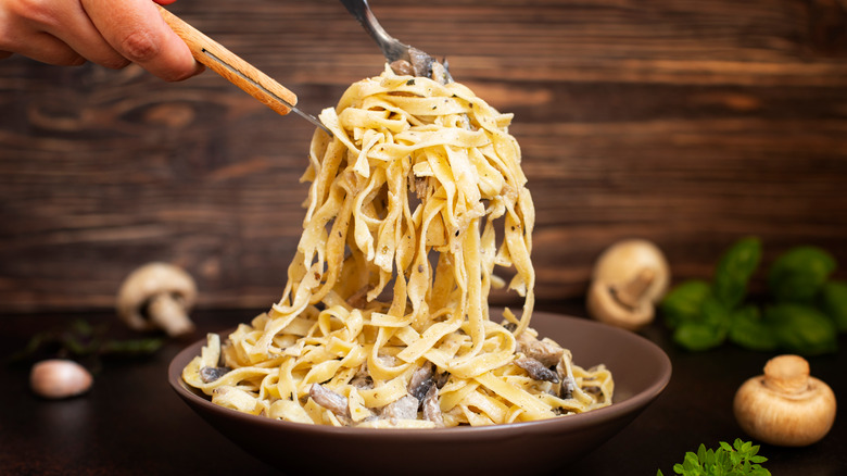 Person scooping fettuccine pasta with forks