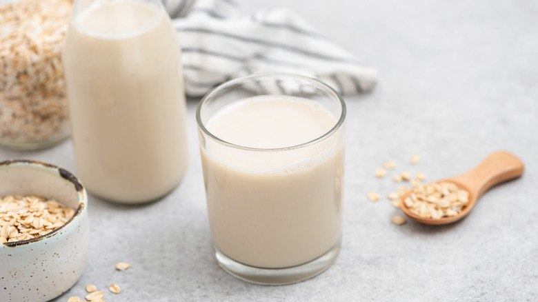 A glass of oat milk next to a bowl and spoon of oats.