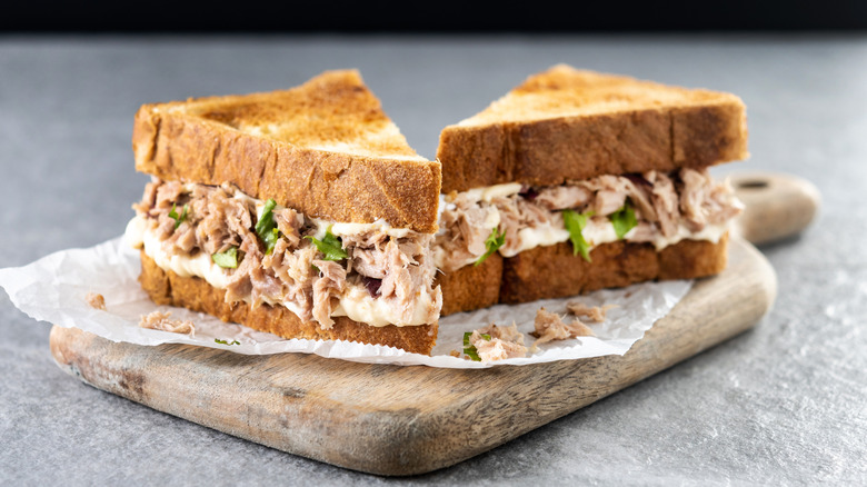Tuna salad sandwich on toast, cut in half, on cutting board