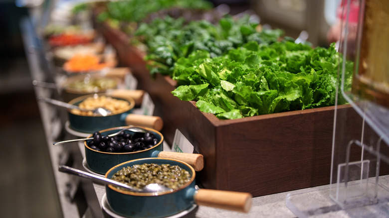 Salad bar with leafy greens and bowls of toppings