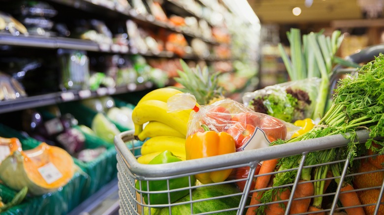 Shopping cart full of produce in front of a refrigerated aisle.