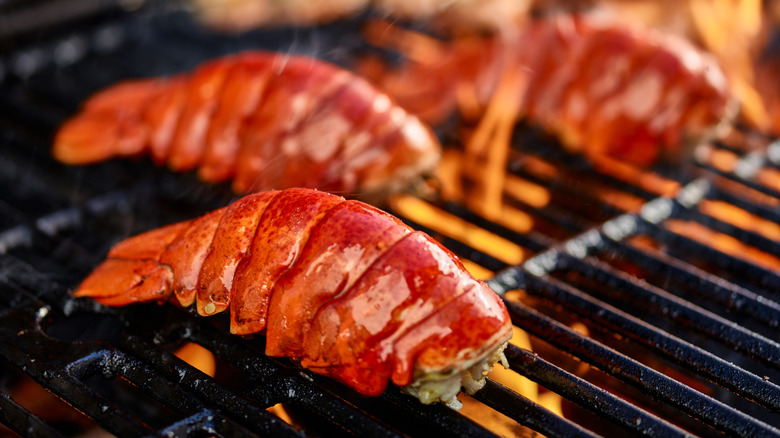 Lobster tails cooking on a grill with open flames.