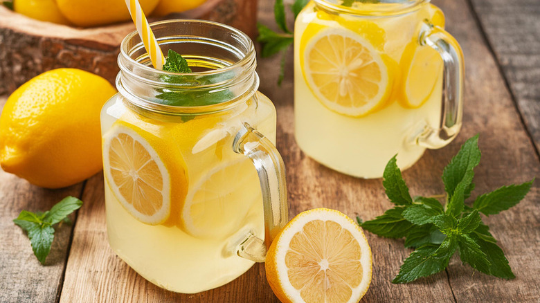 Two glasses of refreshing lemonade cocktails on a table with fresh lemons and mint for garnishing