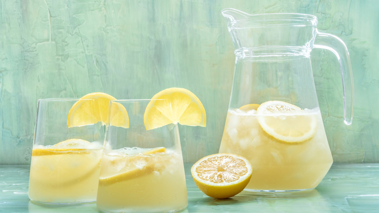 A pitcher of a refreshing lemonade cocktail with two glasses already served and garnished with lemon wedges