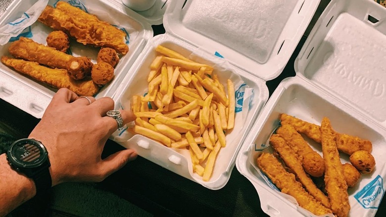 Photo of a person reaching for a fry with fried chicken and fish next to it