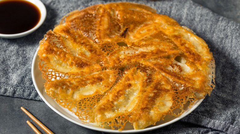 Pan fried dumplings with dumpling skirt next to soy sauce and chopsticks.